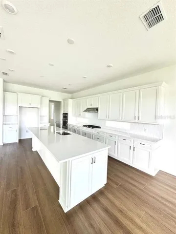 a large white kitchen with kitchen island a sink dishwasher a stove and white cabinets with wooden floor