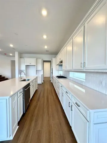 a large kitchen with a large counter top a sink stainless steel appliances and cabinets
