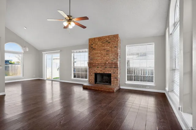 an empty room with wooden floor fireplace and windows