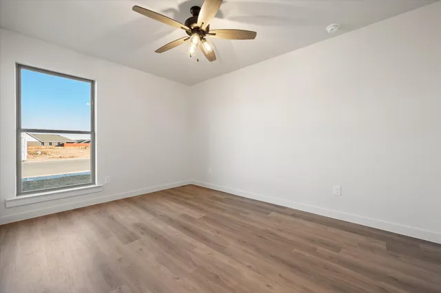 an empty room with wooden floor chandelier fan and windows