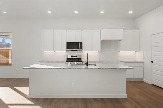 a kitchen with kitchen island granite countertop a sink a stove a microwave a counter top and cabinets