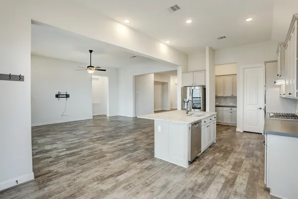 a large white kitchen with kitchen island a stove a sink a refrigerator and white cabinets with wooden floor