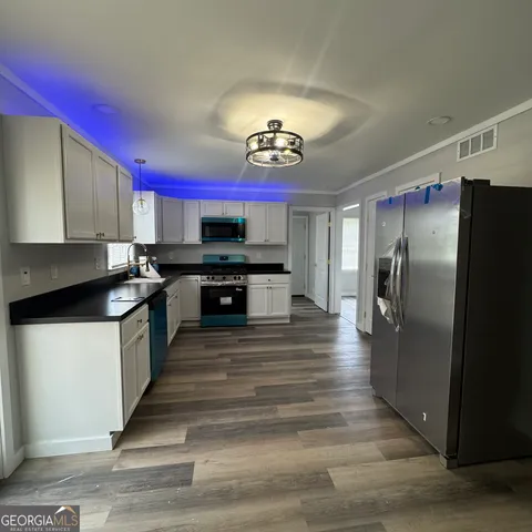 a kitchen with stainless steel appliances kitchen island granite countertop a refrigerator a stove and a sink with wooden floor