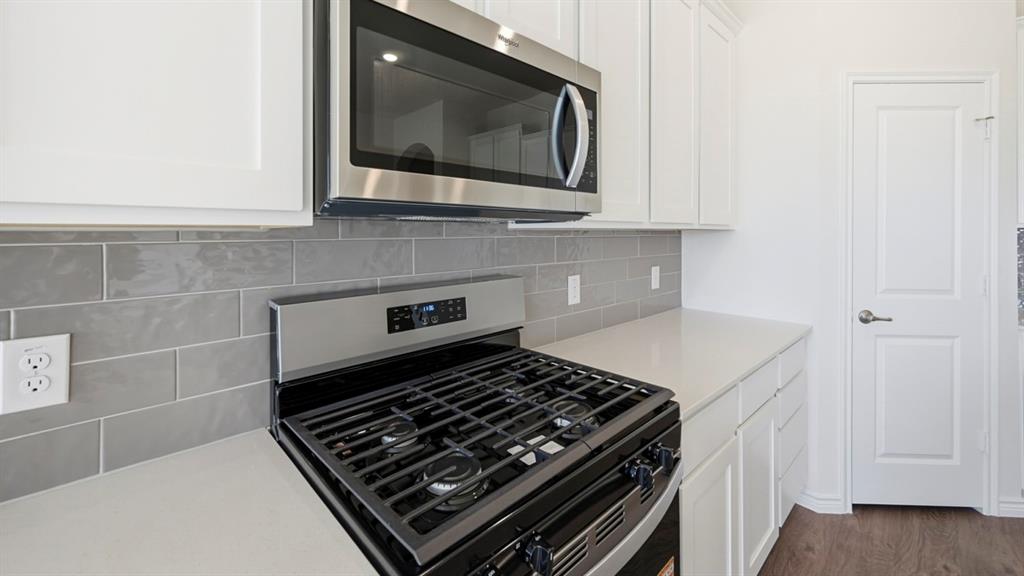 4163 Waldron Trail Forney, TX 75126 - Photo 4 of 30 Stainless steel gas range with coordinating microwave, quartz countertops, and a gray subway tile backsplash