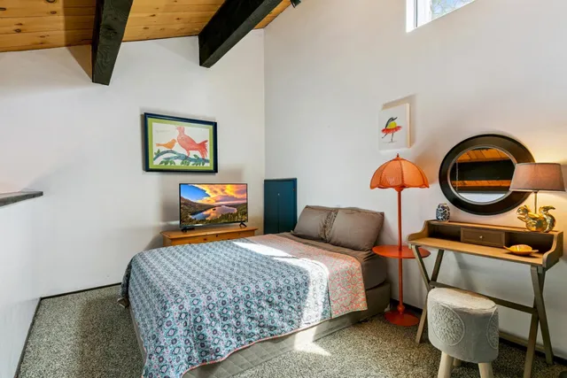 a bedroom with a bed a standing fan and a baby crib