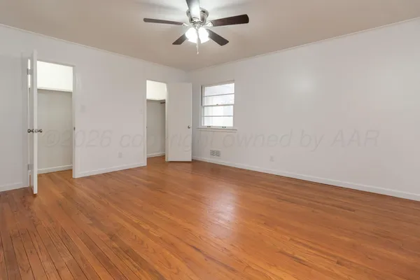 an empty room with wooden floor chandelier fan and windows