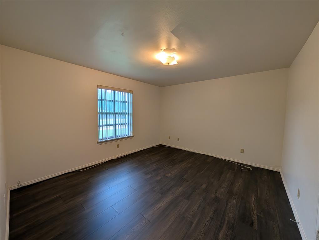 4715 Skillman Street, Unit A Dallas, TX 75206 - Photo 26 of 28 Spacious room featuring dark wood-finish flooring, light-toned walls, a window with horizontal blinds, white baseboards, and a flush-mount ceiling light fixture