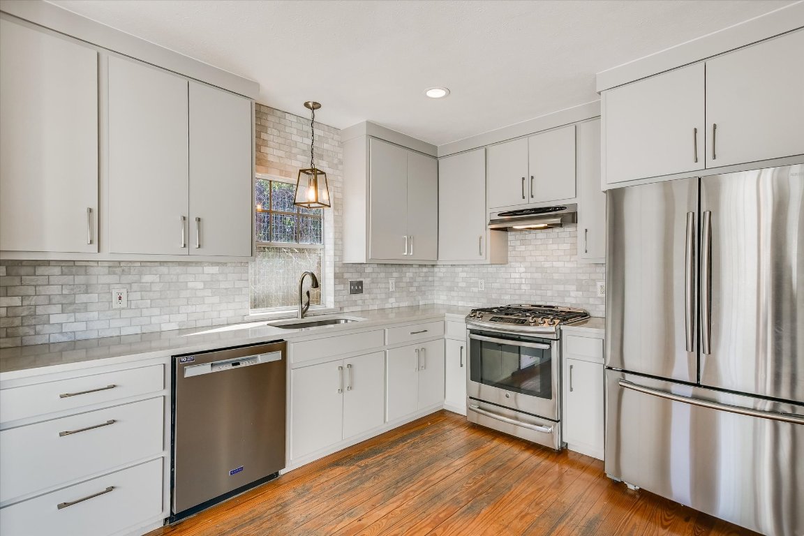 1208 East 13th Street Austin, TX 78702 - Photo 5 of 12 Kitchen with stainless steel appliances, pendant lighting, under cabinet range hood, light wood-style floors, and decorative backsplash