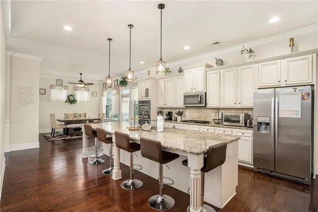 a large kitchen with stainless steel appliances kitchen island granite countertop a stove a refrigerator a oven and white cabinets with wooden floor