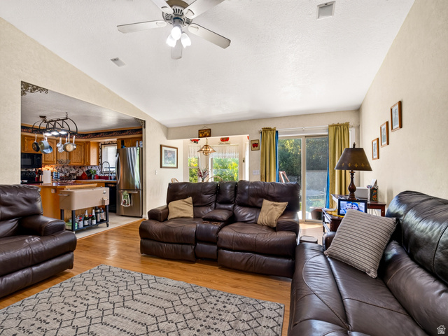 4380 Main Street Logan, UT 84321 - Photo 18 of 74 Family room with vaulted ceiling, ceiling fan, LVP flooring, and view of kitchen with wood cabinetry and stainless steel appliances, sliding glass door to exterior