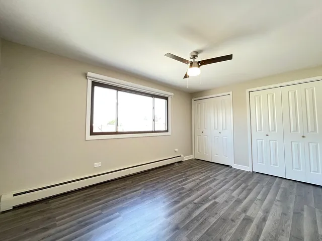 an empty room with wooden floor ceiling fan and windows