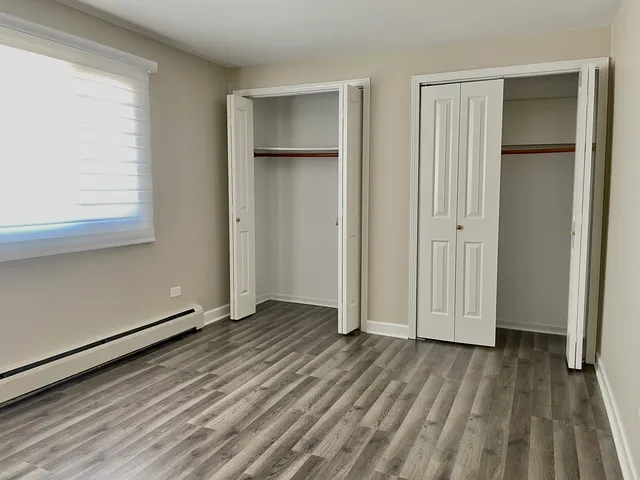an empty room with wooden floor closet and windows