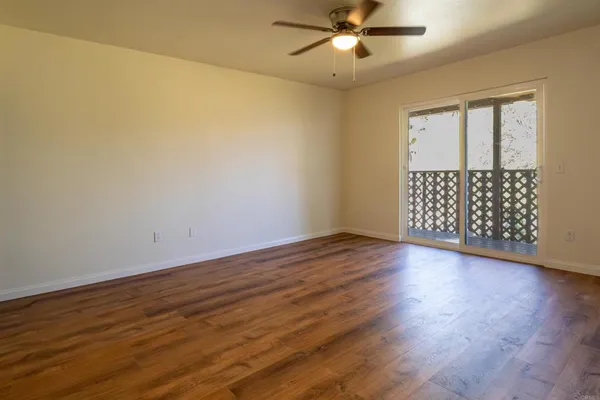 an empty room with wooden floor fan and windows