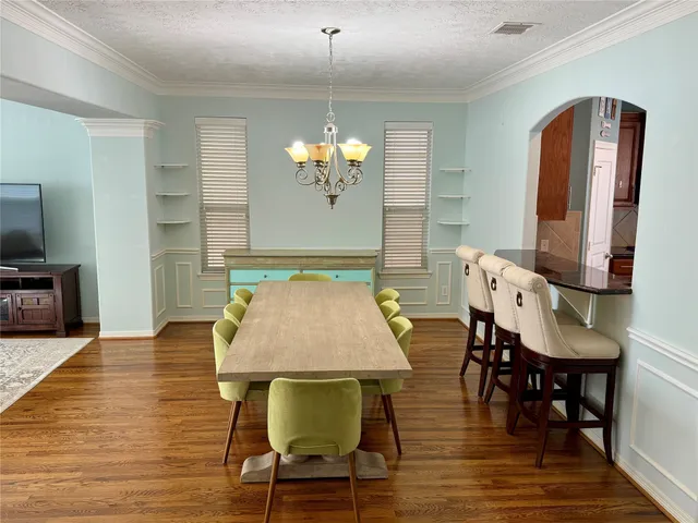 a dining room with wooden floor a chandelier a glass table and chairs