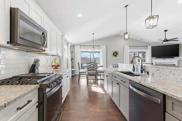 a kitchen with stainless steel appliances kitchen island granite countertop a dining table chairs and white cabinets