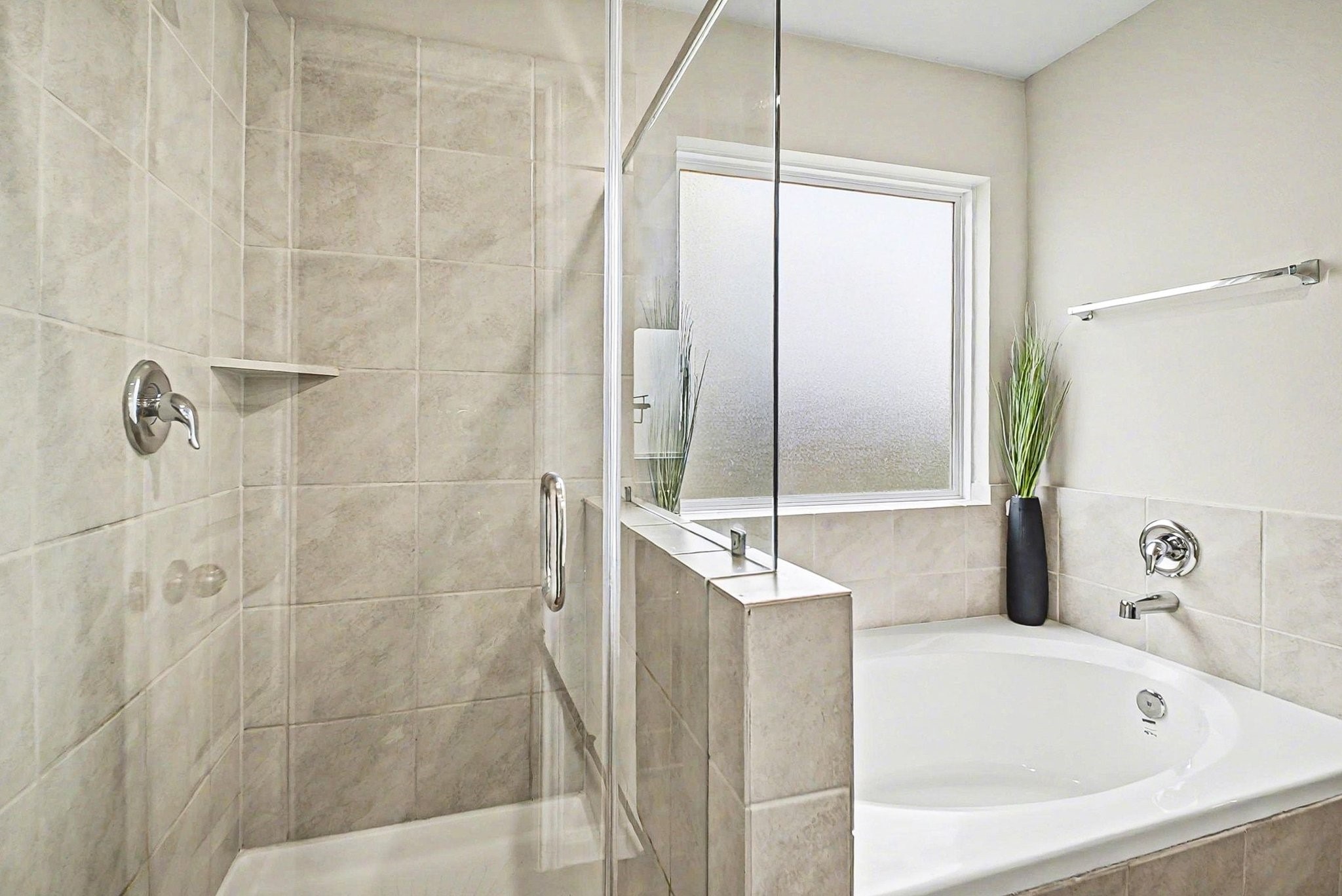 4906 Luke Matthew Drive Rosharon, TX 77583 - Photo 15 of 34 The primary bathroom features a sleek design with a glass-enclosed shower and a separate bathtub. Neutral tilework complements a large frosted window, allowing natural light while maintaining privacy.