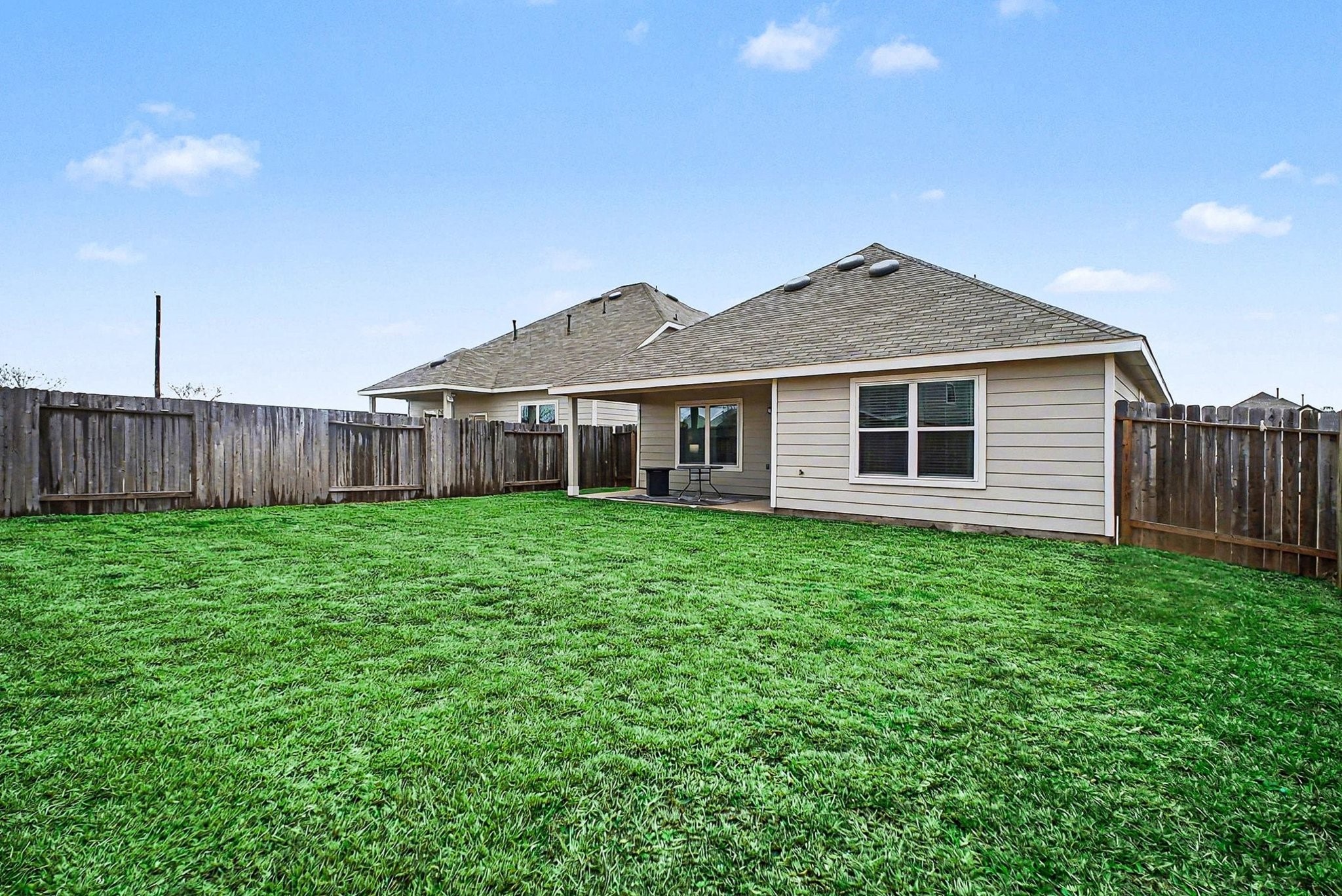 4906 Luke Matthew Drive Rosharon, TX 77583 - Photo 26 of 34 Spacious backyard with well-maintained grass, enclosed by a wooden fence. The house features a covered patio area, ideal for outdoor relaxation or entertaining.