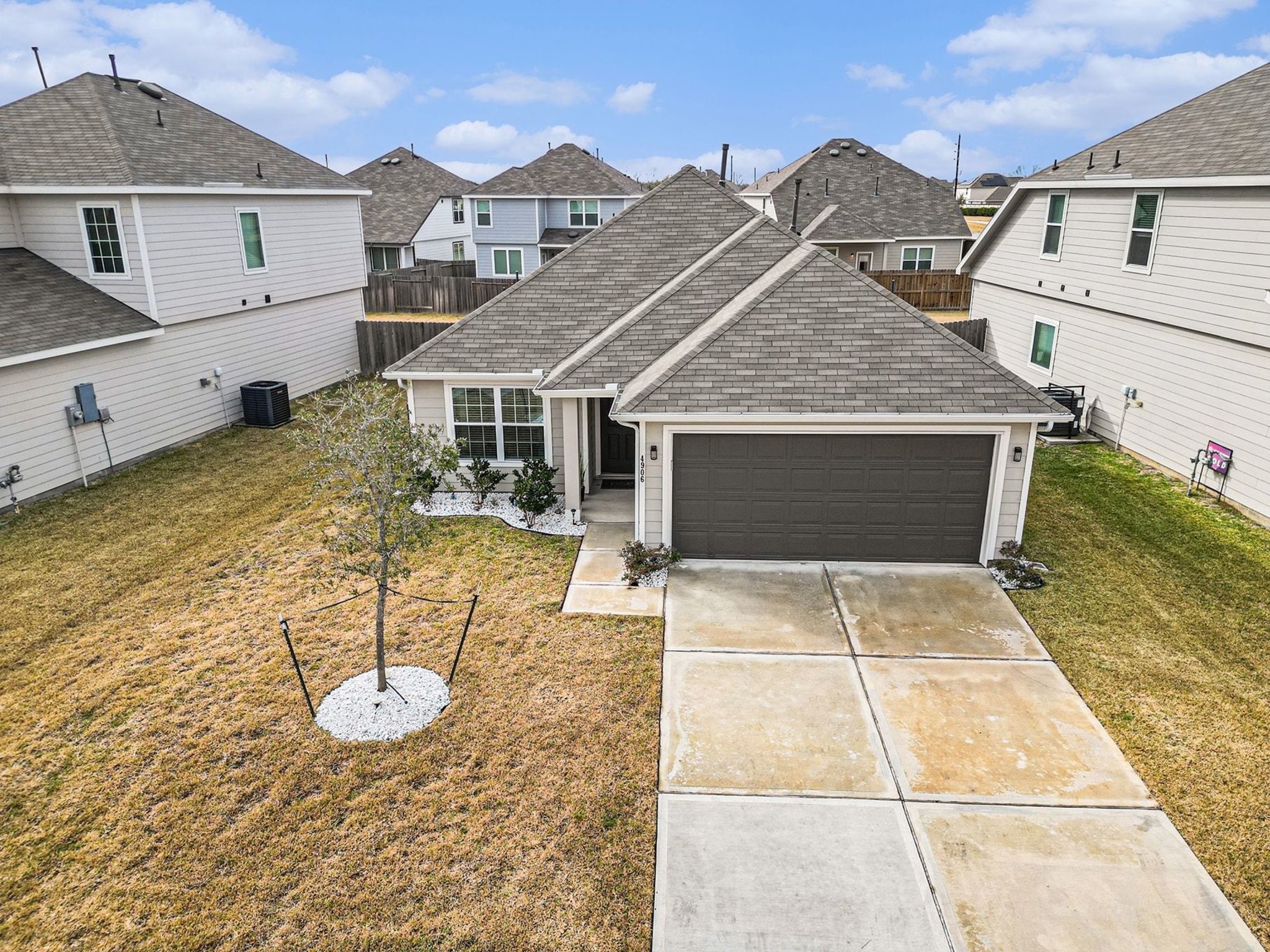 4906 Luke Matthew Drive Rosharon, TX 77583 - Photo 27 of 34 modern single-story home with a two-car garage, a neatly landscaped front yard, and a small tree. The house has a gray exterior with a gabled roof and is situated in a recently completed suburban neighborhood.