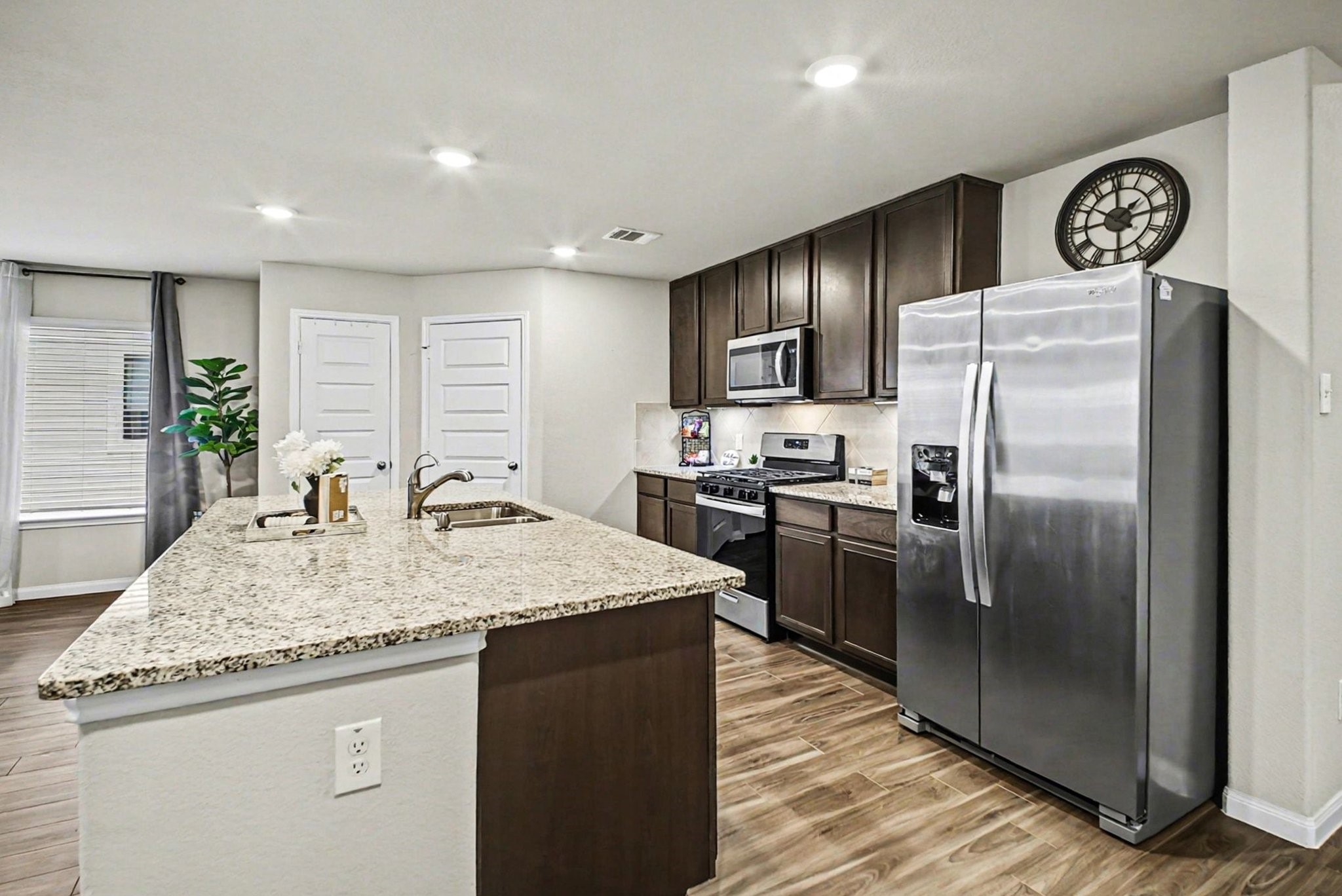 4906 Luke Matthew Drive Rosharon, TX 77583 - Photo 6 of 34 This modern kitchen features granite countertops, stainless steel appliances, and dark wood cabinetry. It includes a spacious island with a sink and is well-lit with recessed lighting. The open layout offers a view of the adjacent room, enhancing the home's flow.