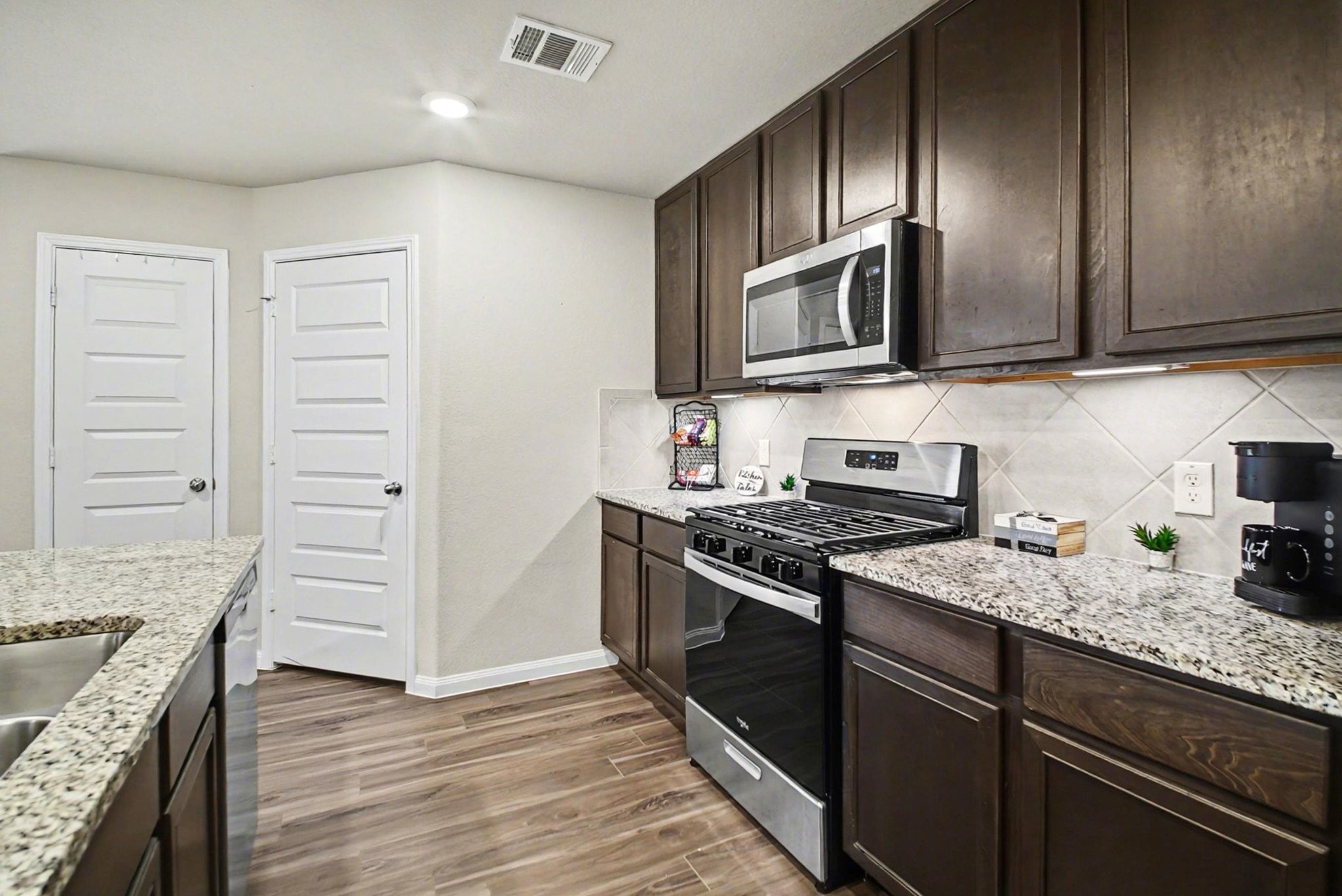4906 Luke Matthew Drive Rosharon, TX 77583 - Photo 7 of 34 This kitchen features modern stainless steel appliances, dark wood cabinetry, and granite countertops. It has a sleek tile backsplash and wood-look flooring, creating a warm and inviting space.