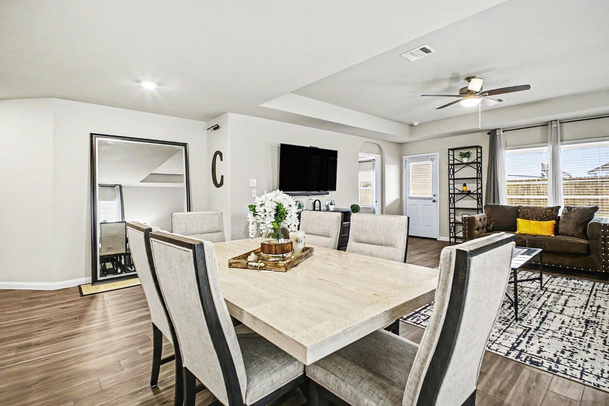 4906 Luke Matthew Drive Rosharon, TX 77583 - Photo 10 of 34 This open-concept living and dining area features a modern dining table, comfortable seating, and abundant natural light from large windows. The space is accented with a stylish ceiling fan, hardwood floors, and a wall-mounted TV, creating a cozy yet elegant atmosphere.