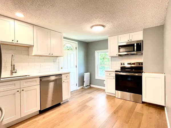 a kitchen with stainless steel appliances white cabinets a sink a stove a microwave and wooden floors