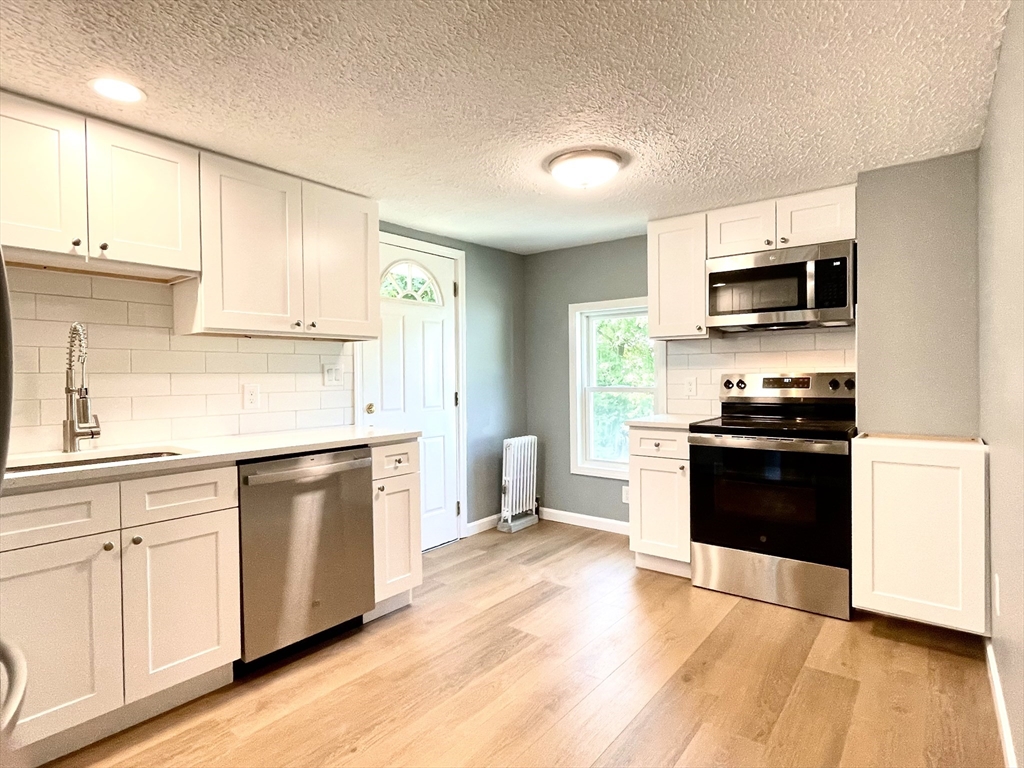a kitchen with stainless steel appliances white cabinets a sink a stove a microwave and wooden floors