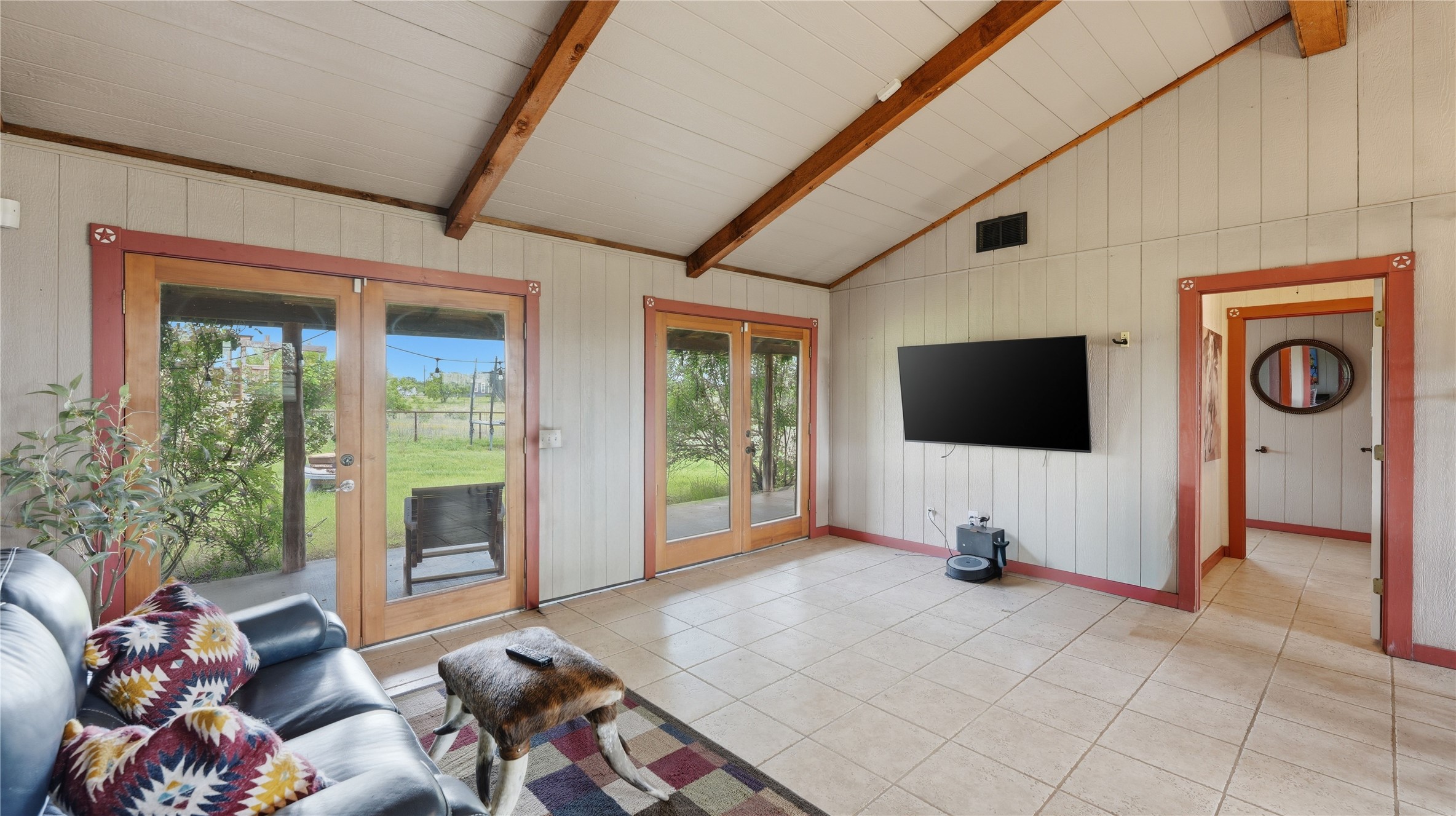 127 Offer Llano, TX 78643 - Photo 32 of 40 Vaulted ceiling with exposed wood beams, dual glass-paned doors, tile flooring, and wall-mounted television bracket