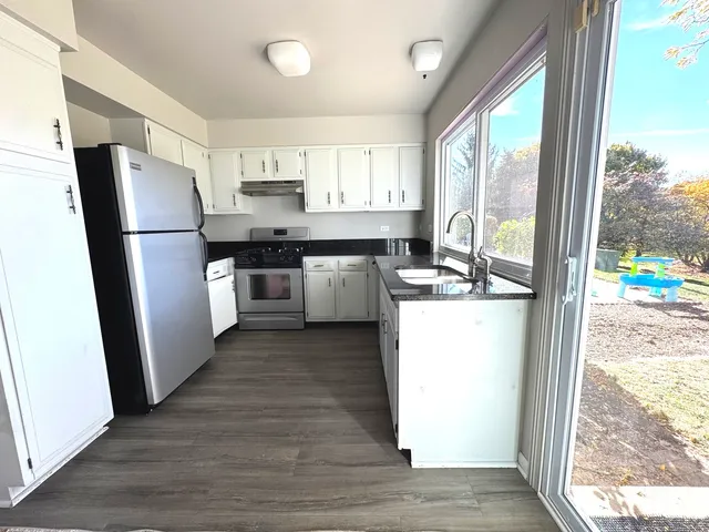 a kitchen with stainless steel appliances granite countertop a refrigerator a stove a sink and a large window