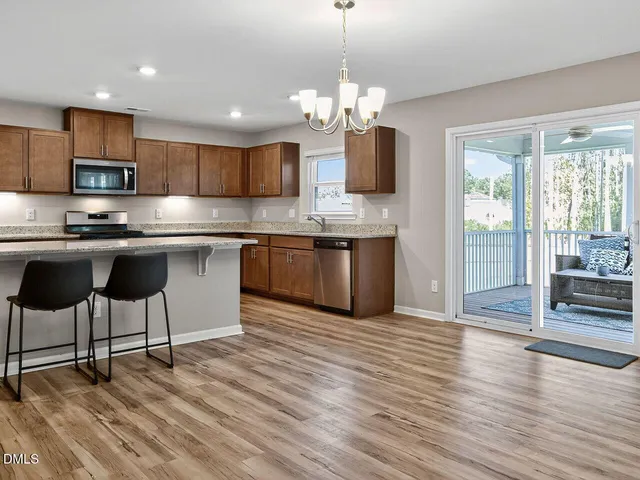 a kitchen with stainless steel appliances kitchen island granite countertop a stove top oven a sink dishwasher a dining table and chairs with wooden floor