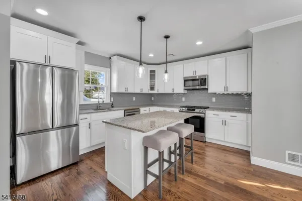 a kitchen with stainless steel appliances granite countertop a refrigerator a sink a stove a microwave and white cabinets with wooden floor