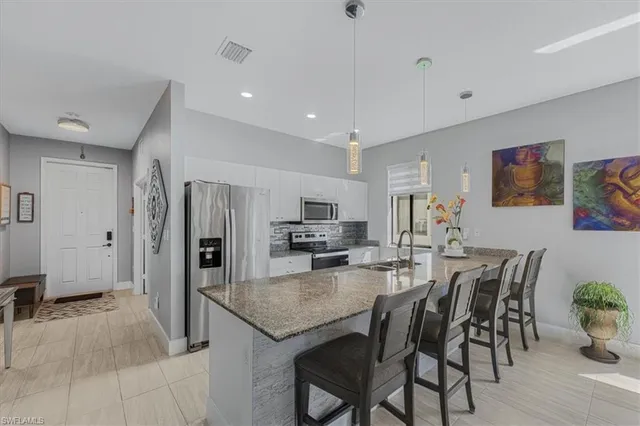 a kitchen with stainless steel appliances granite countertop a dining table chairs refrigerator and sink
