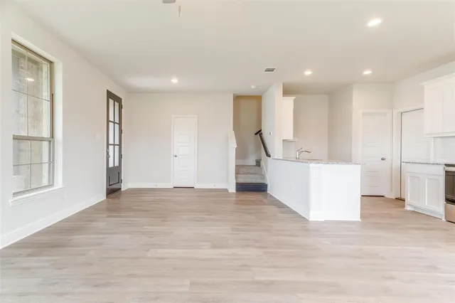 a view of an empty room with wooden floor and a kitchen