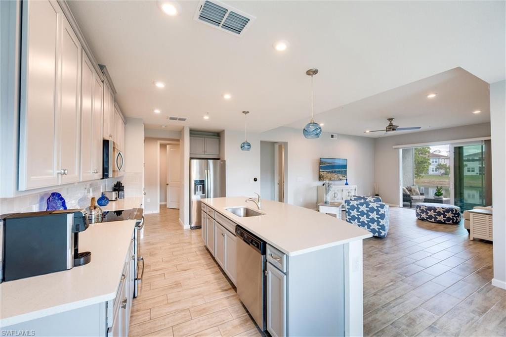 4607 Arboretum Circle, Unit 103 Naples, FL 34112 - Photo 29 of 29 a large living room with stainless steel appliances kitchen island a large counter top space a sink wooden floor and windows