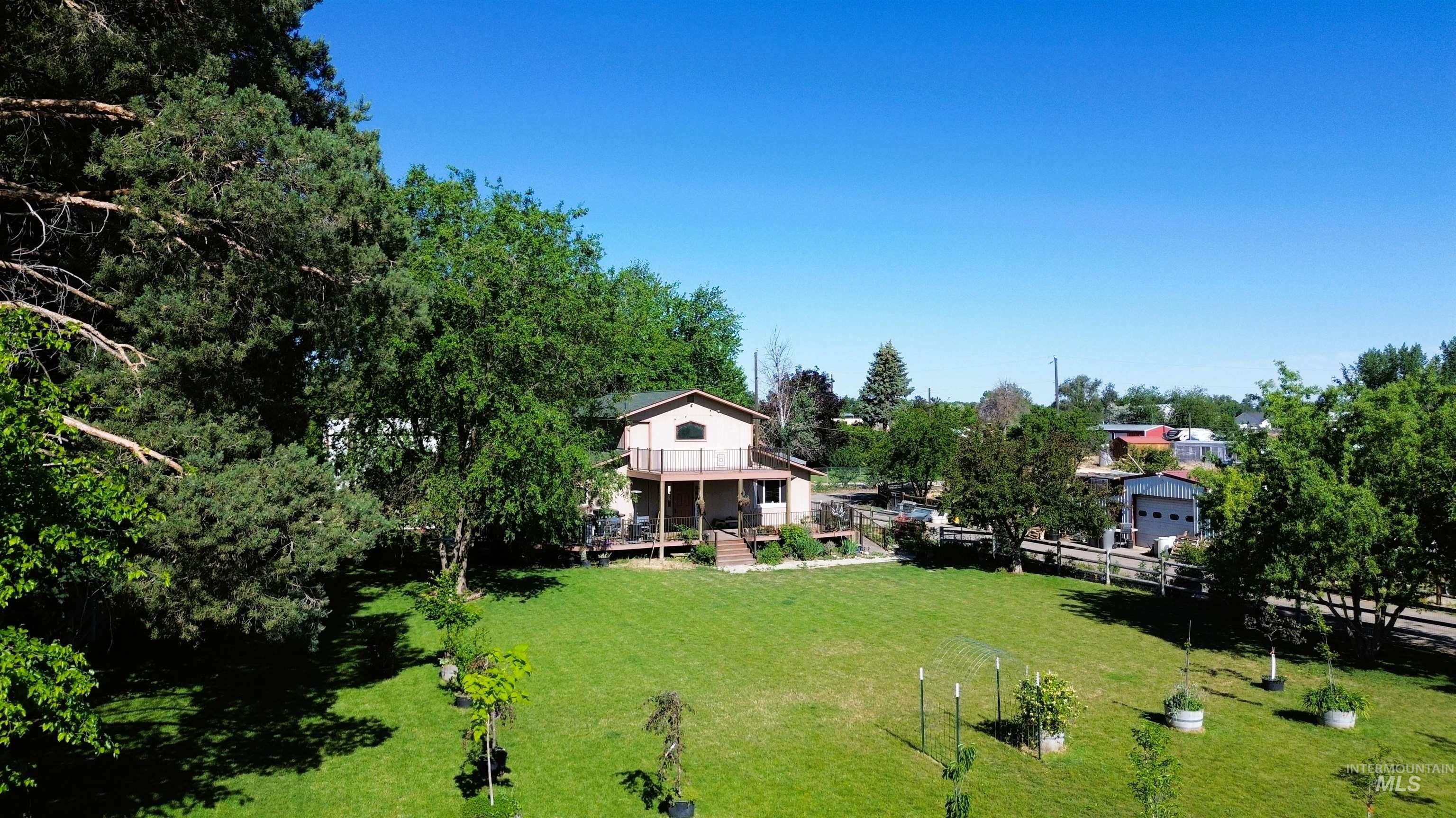 16985 Garnet Road Wilder, ID 83676 - Photo 38 of 39 Expansive green lawn with mature trees and a two-story residence featuring a second-level balcony and a ground-level deck