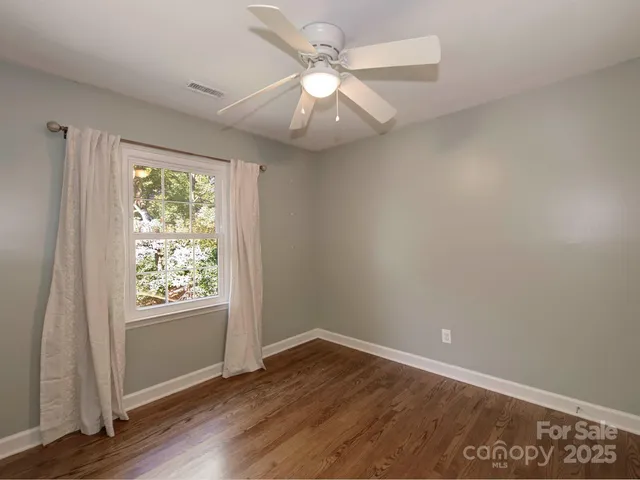 an empty room with wooden floor chandelier fan and windows
