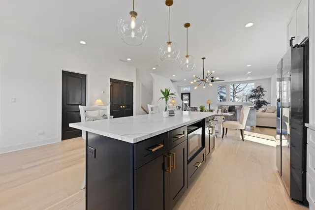 a kitchen with stainless steel appliances kitchen island granite countertop a refrigerator a sink dishwasher and white cabinets with wooden floor