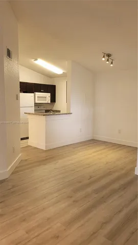 a view of kitchen and empty room with wooden floor