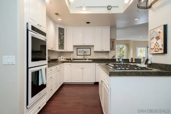 a white kitchen with stainless steel appliances granite countertop a stove a sink and a microwave