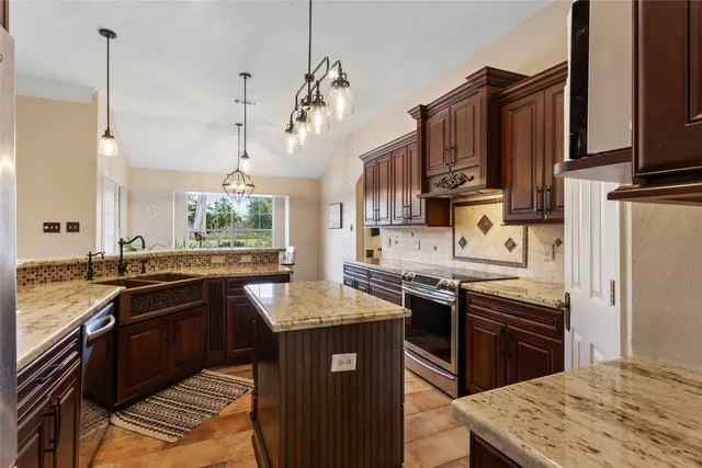 a kitchen with stainless steel appliances granite countertop a sink a stove top oven a refrigerator cabinets and wooden floor