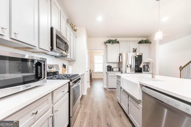 a kitchen with stainless steel appliances a sink dishwasher a stove top oven a refrigerator with white cabinets and wooden floor