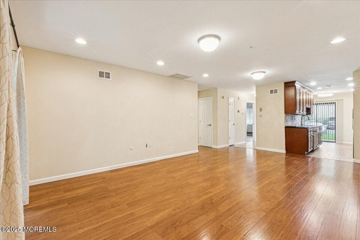 70 Overlook Way, Unit E Manalapan, NJ 07726 - Photo 9 of 21 an empty room with wooden floor and a kitchen view