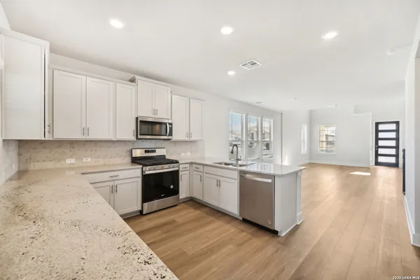 a kitchen with stainless steel appliances granite countertop a stove top oven a sink dishwasher and a refrigerator with wooden floor