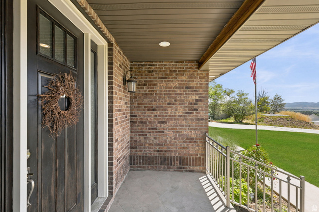 580 North 300 East Logan, UT 84321 - Photo 22 of 74 Covered front porch featuring brick siding, a dark wood-finish entry door, an overhead light fixture, and a metal handrail