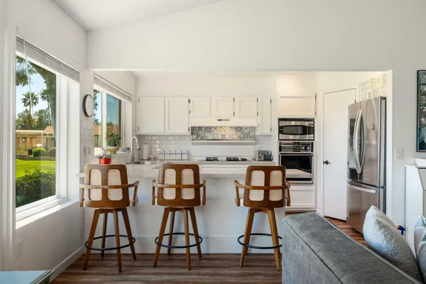 a kitchen with stainless steel appliances granite countertop a stove top oven a refrigerator a dining table and chairs with wooden floor