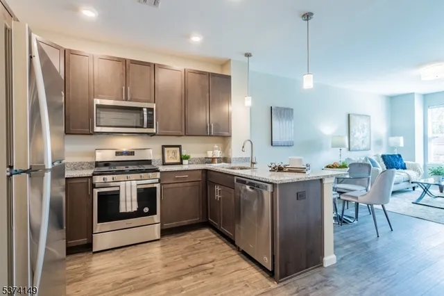 a kitchen with stainless steel appliances granite countertop a stove top oven a sink dishwasher a refrigerator and a dining table with wooden floor