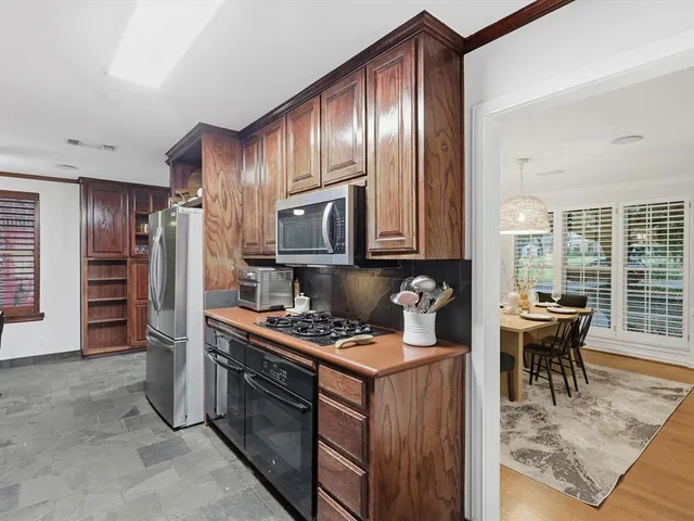 a kitchen with stainless steel appliances granite countertop a stove top oven a refrigerator a dining table and chairs with wooden floor