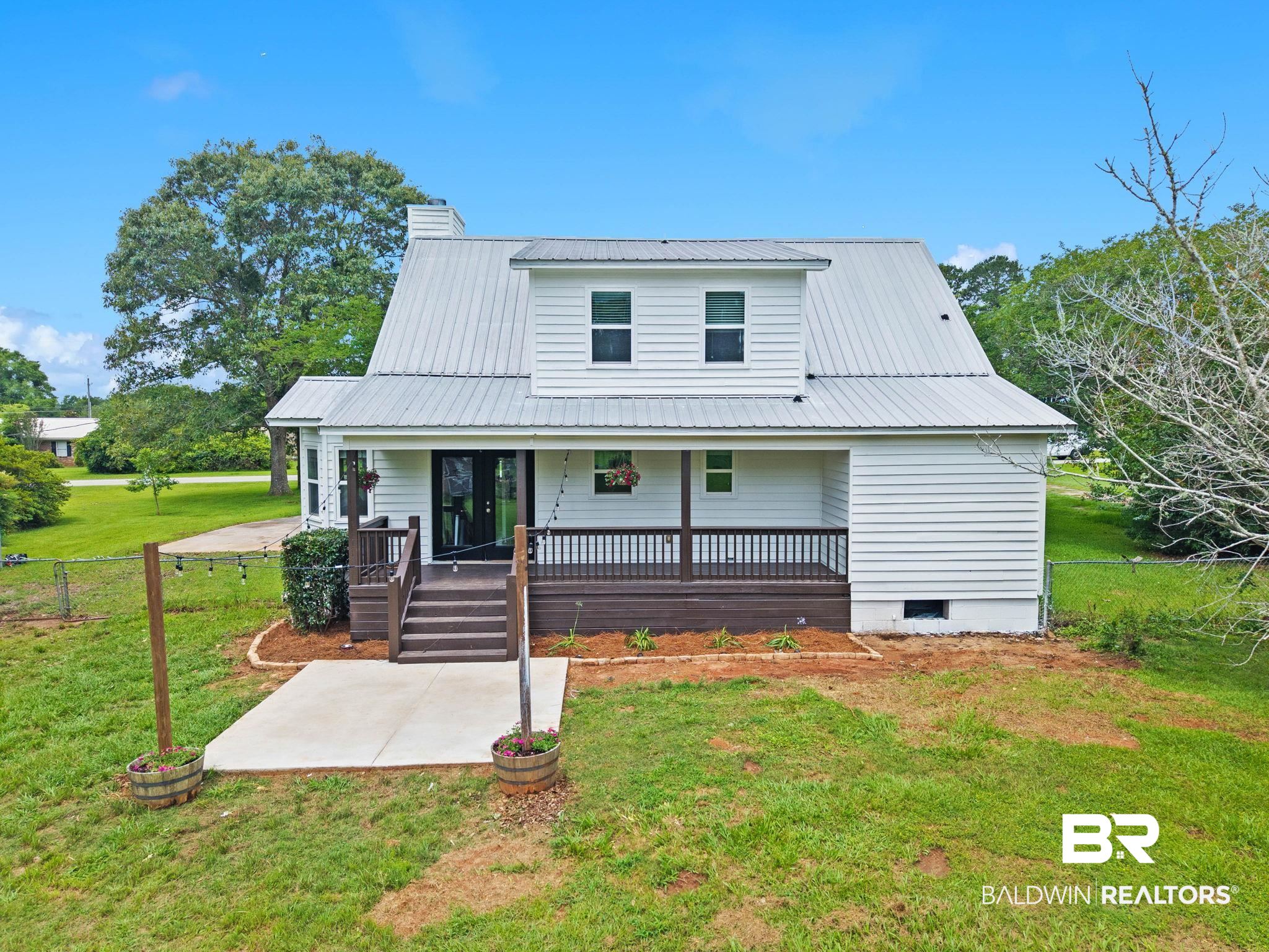 22810 High Ridge Road Fairhope, AL 36532 - Photo 5 of 78 White siding exterior with a metal roof, featuring a covered wooden deck, dual-pane windows, and a ground-level concrete patio
