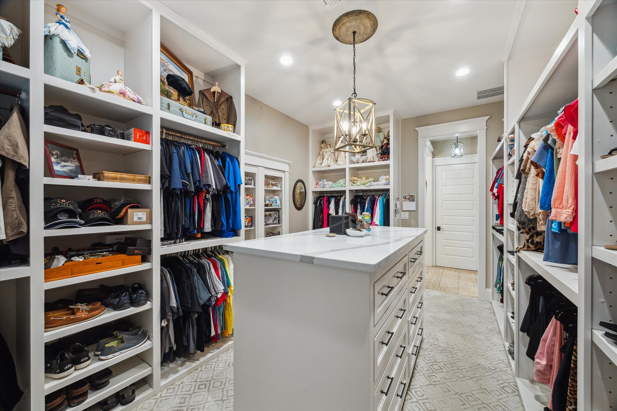 1255 Bronco Trail Angleton, TX 77515 - Photo 20 of 50 The primary closet offers a refined touch with custom high-end designer carpeting, built-in shelving, and a built-in dresser with sleek quartz countertops. A stylish sitting bench provides a convenient space to relax or get ready, while an elegant chandelier casts a warm glow, completing the luxurious feel of this well-appointed closet.