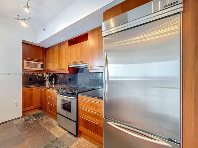 a kitchen with stainless steel appliances granite countertop a refrigerator a stove and a sink with wooden floor